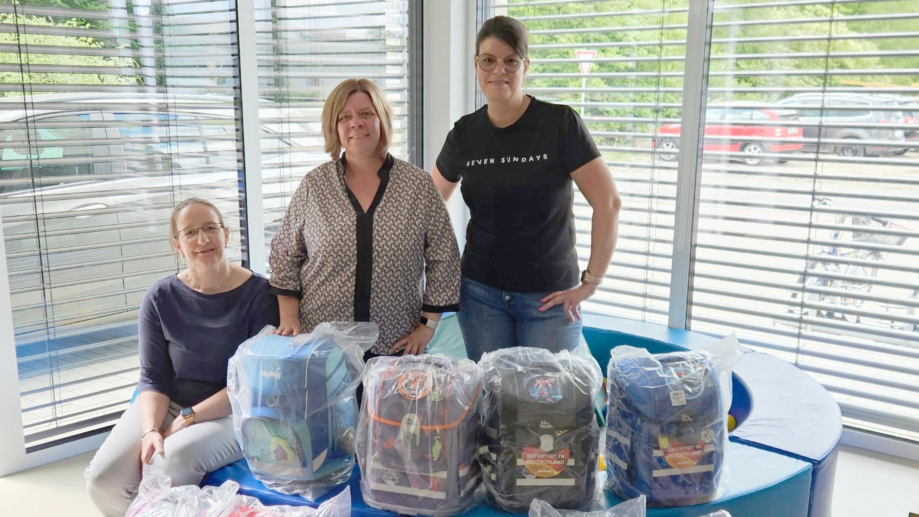 Daniela Brillert, Ramona Rensing und Marlene Terbeck stehen hinter 10 gespendeten Schultornistern.