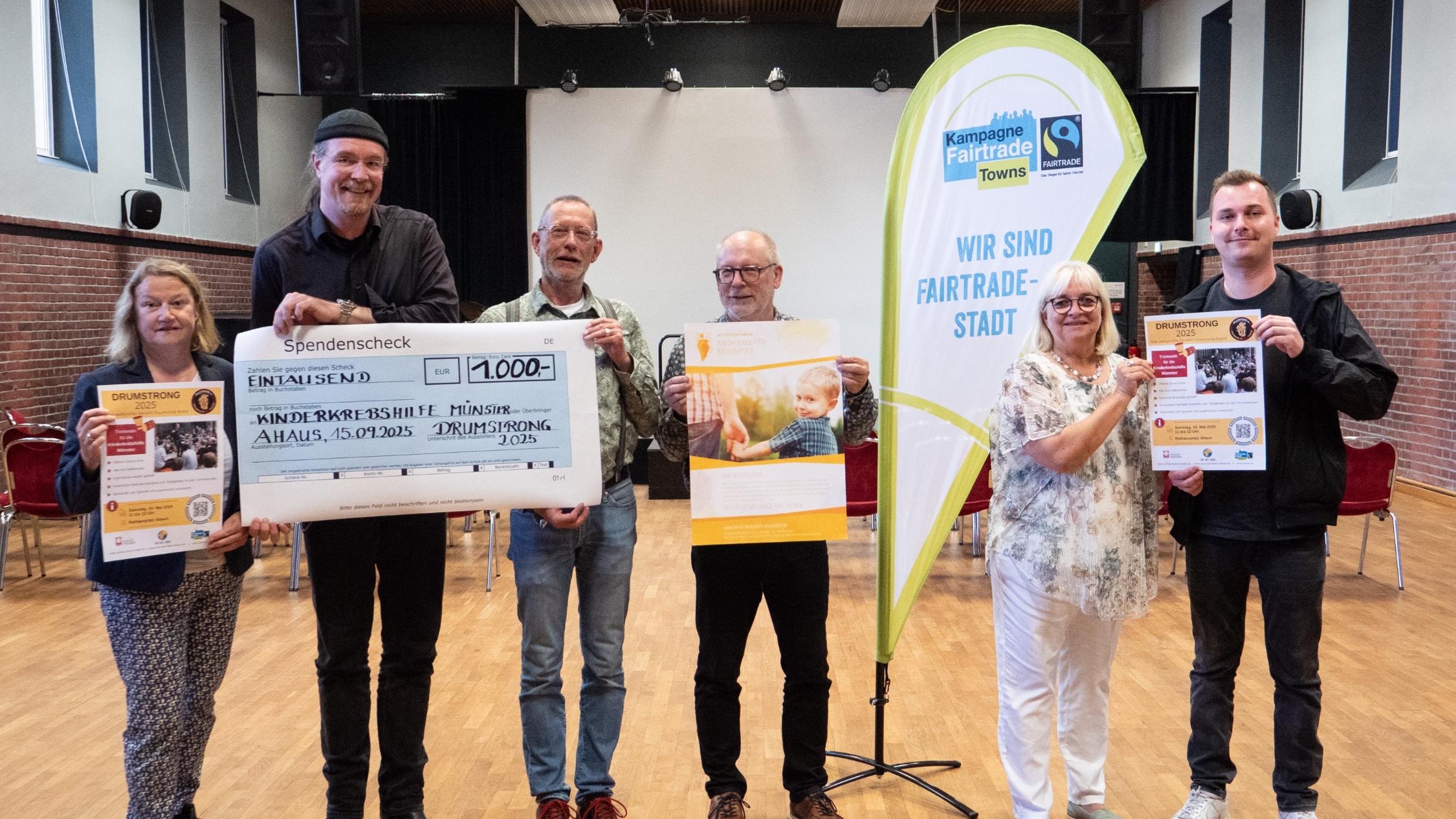 Sechs Personen halten Plakate und einen symbolischen Scheck in die Kamera. Auf dem Scheck ist eine Spendensumme von 1000 Euro eingetragen.